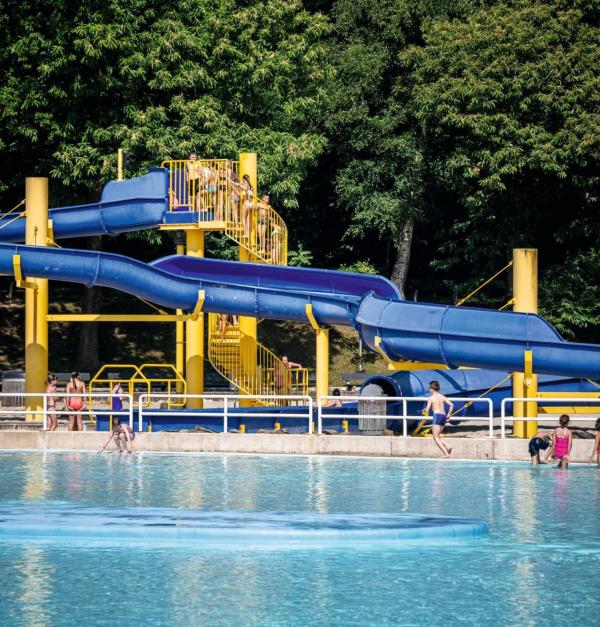 Een buitenzwembad met helder blauw water en een grote kronkelende glijbaan, ondersteund door gele pilaren.